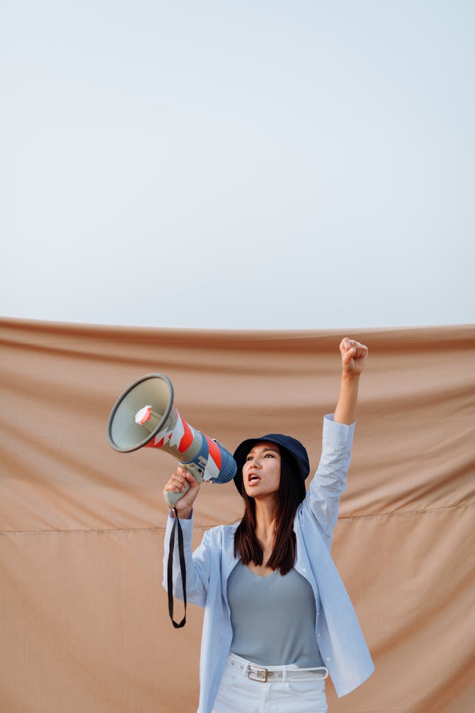 Asian woman passionately protesting with a megaphone while raising her fist.